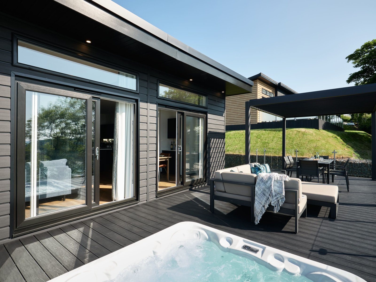 Private luxury lodge terrace overlooking the Taf Estuary, furnished with outdoor sofas, sun loungers and a hot tub.