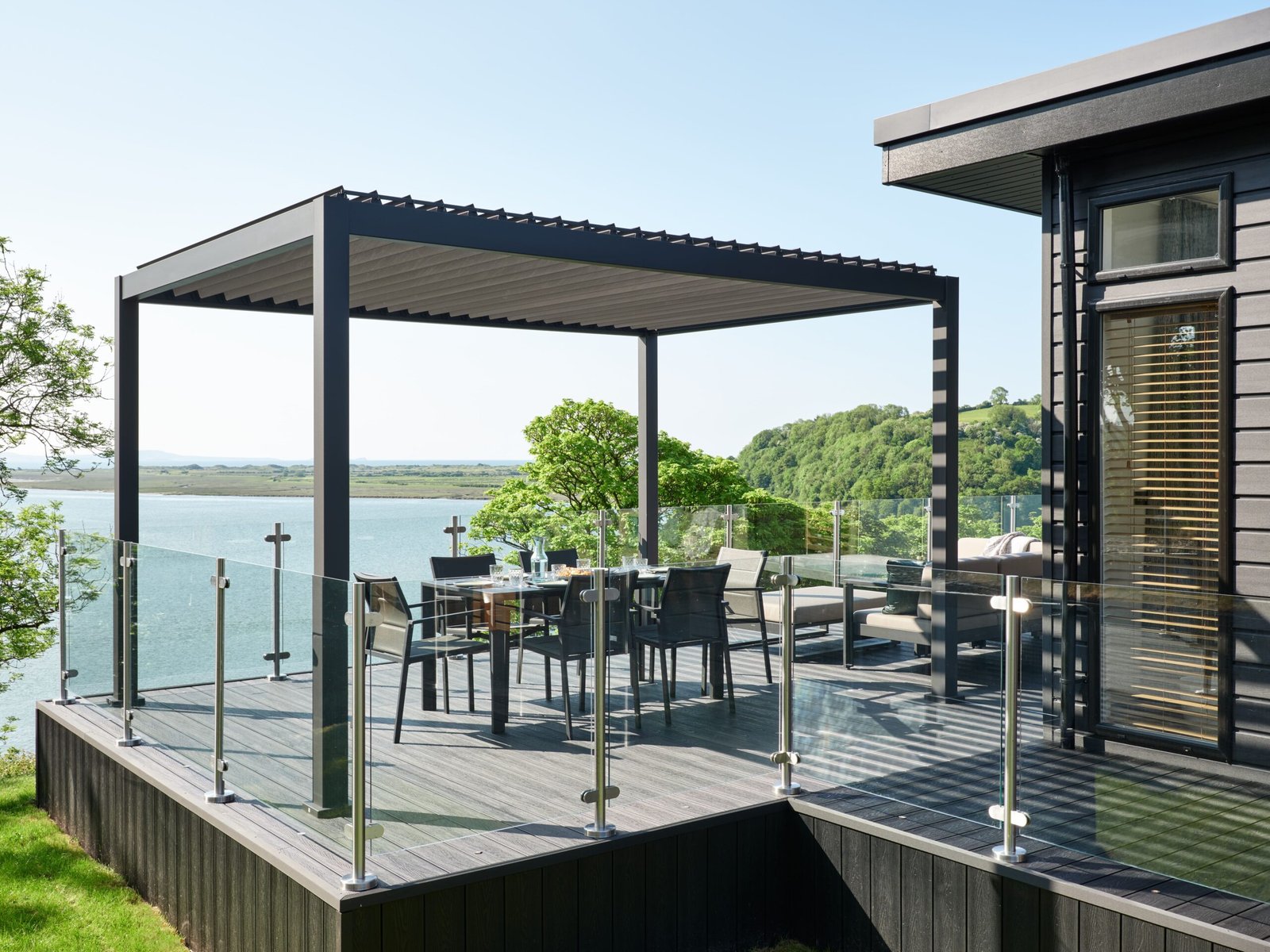 Luxury lodge terrace with pergola, outdoor dining furniture and glass balustrades overlooking the estuary at Dylan Coastal Resort.
