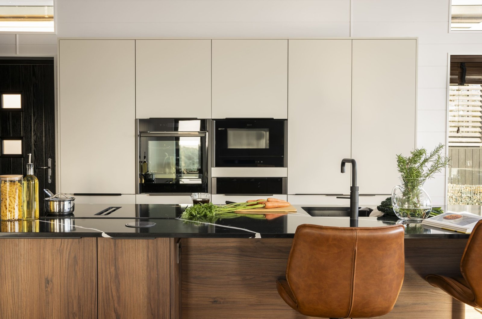 Modern luxury lodge kitchen with black stone island, integrated appliances, pale cabinetry and tan leather breakfast bar chairs.
