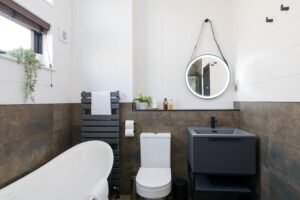 Contemporary holiday lodge bathroom with white freestanding bath, black vanity unit and illuminated circular mirror.