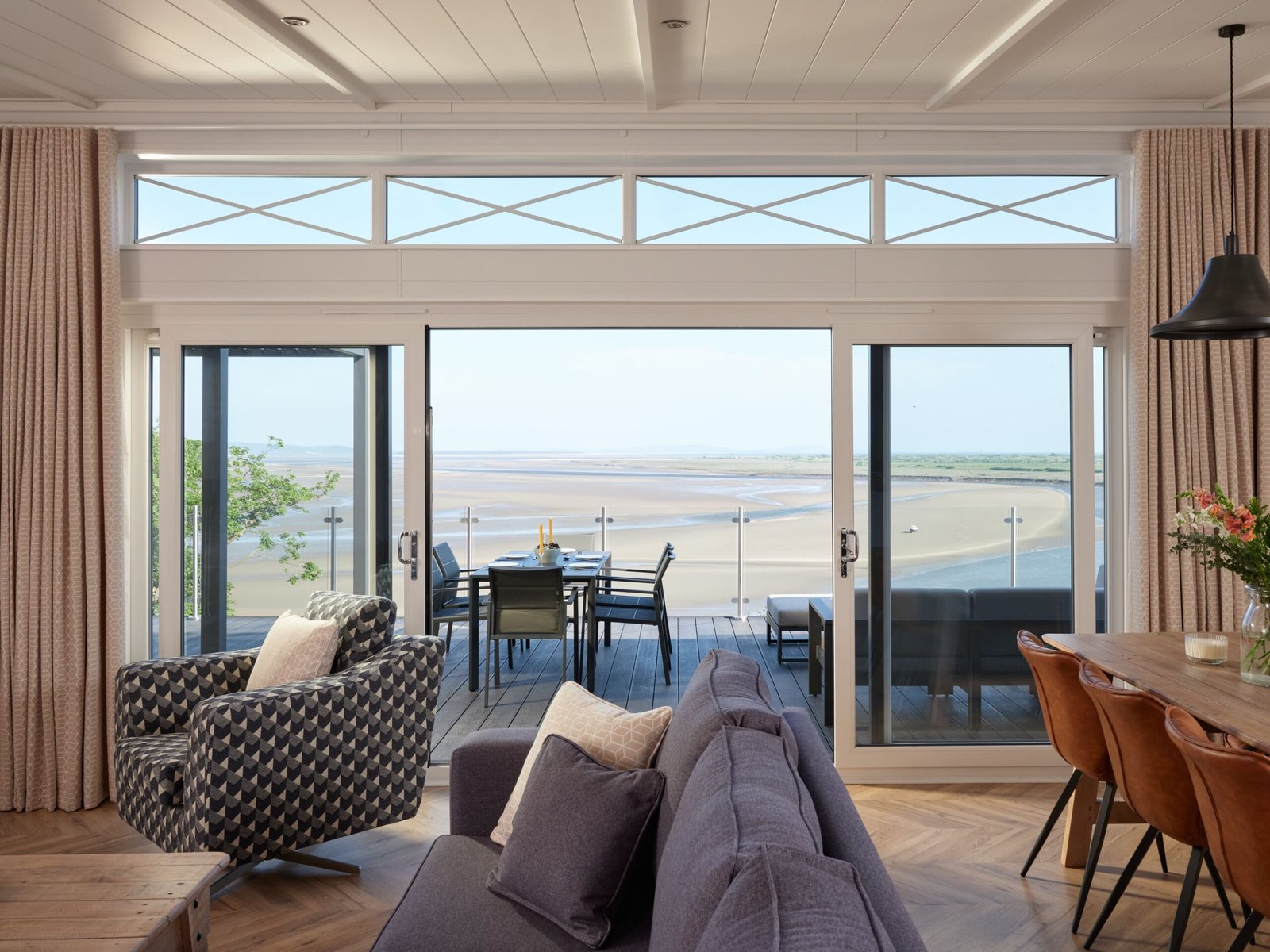 Open-plan luxury lodge lounge with sliding glass doors leading to a private terrace overlooking the Taf Estuary.