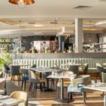 Interior of Milk Wood Bar and Kitchen with upholstered restaurant seating, pendant lighting and an open dining area.