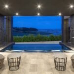 Hydrotherapy pool at Milk Wood Spa overlooking the Taf Estuary at dusk, with lounge seating and dark stone walls.