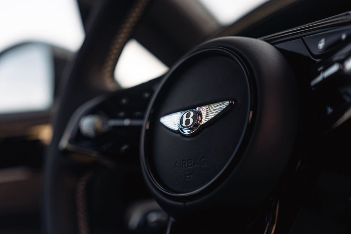 Close-up of the Bentley winged emblem on the black leather steering wheel of the Torcal electric SUV.