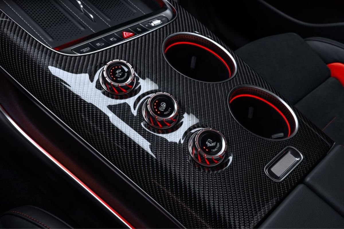 Close-up of the Mercedes-AMG GT SUV carbon-fibre centre console with three rotary driving controls and illuminated cupholders.