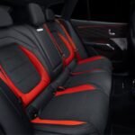 Rear passenger seating in the Mercedes-AMG GT SUV with black upholstery, red inserts and contrasting red seatbelts.