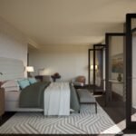 Spacious luxury bedroom with an upholstered bed, wooden furniture and glass doors opening onto a private balcony.
