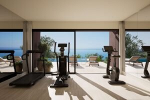Private gym at Rocco Forte Verdura in Sicily, featuring fitness equipment and floor-to-ceiling windows overlooking an infinity pool and the Mediterranean Sea.