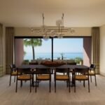Elegant villa dining room with a contemporary chandelier and large glass doors overlooking the Mediterranean Sea.