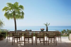 Outdoor dining terrace with a wooden table and chairs overlooking the Mediterranean coastline at Verdura Resort.