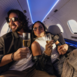 Two passengers seated inside a SyberJet private jet cabin enjoying drinks beneath blue ambient lighting.