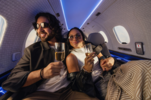 Two passengers seated inside a SyberJet private jet cabin enjoying drinks beneath blue ambient lighting.