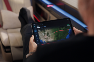 Passenger inside a SyberJet cabin holding a tablet displaying a flight route across the United States.