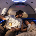 Passengers relaxing inside a SyberJet private jet cabin with reclining seating and blue ambient lighting.