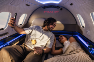 Passengers relaxing inside a SyberJet private jet cabin with reclining seating and blue ambient lighting.