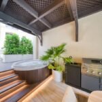 Private outdoor Jacuzzi with timber decking, illuminated steps and a built-in barbecue beneath a pergola.