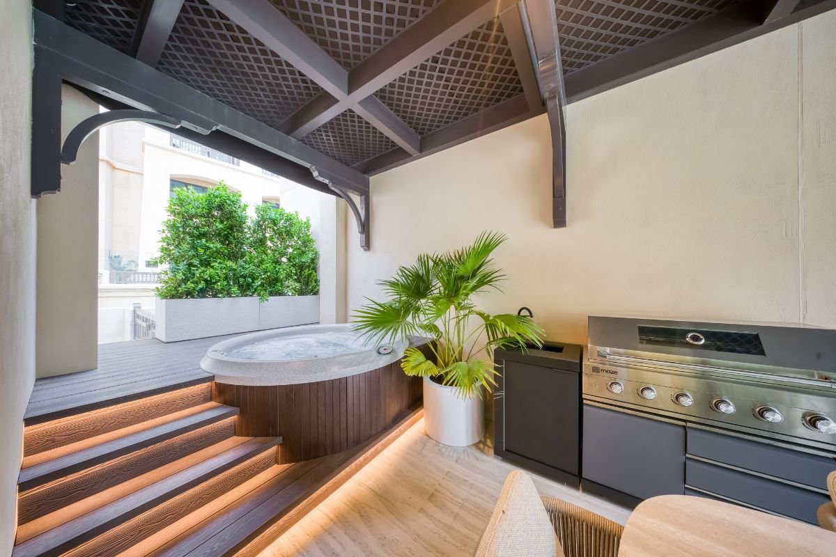 Private outdoor Jacuzzi with timber decking, illuminated steps and a built-in barbecue beneath a pergola.