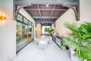 Contemporary covered dining area with white woven chairs, tropical planting and an outdoor kitchen.