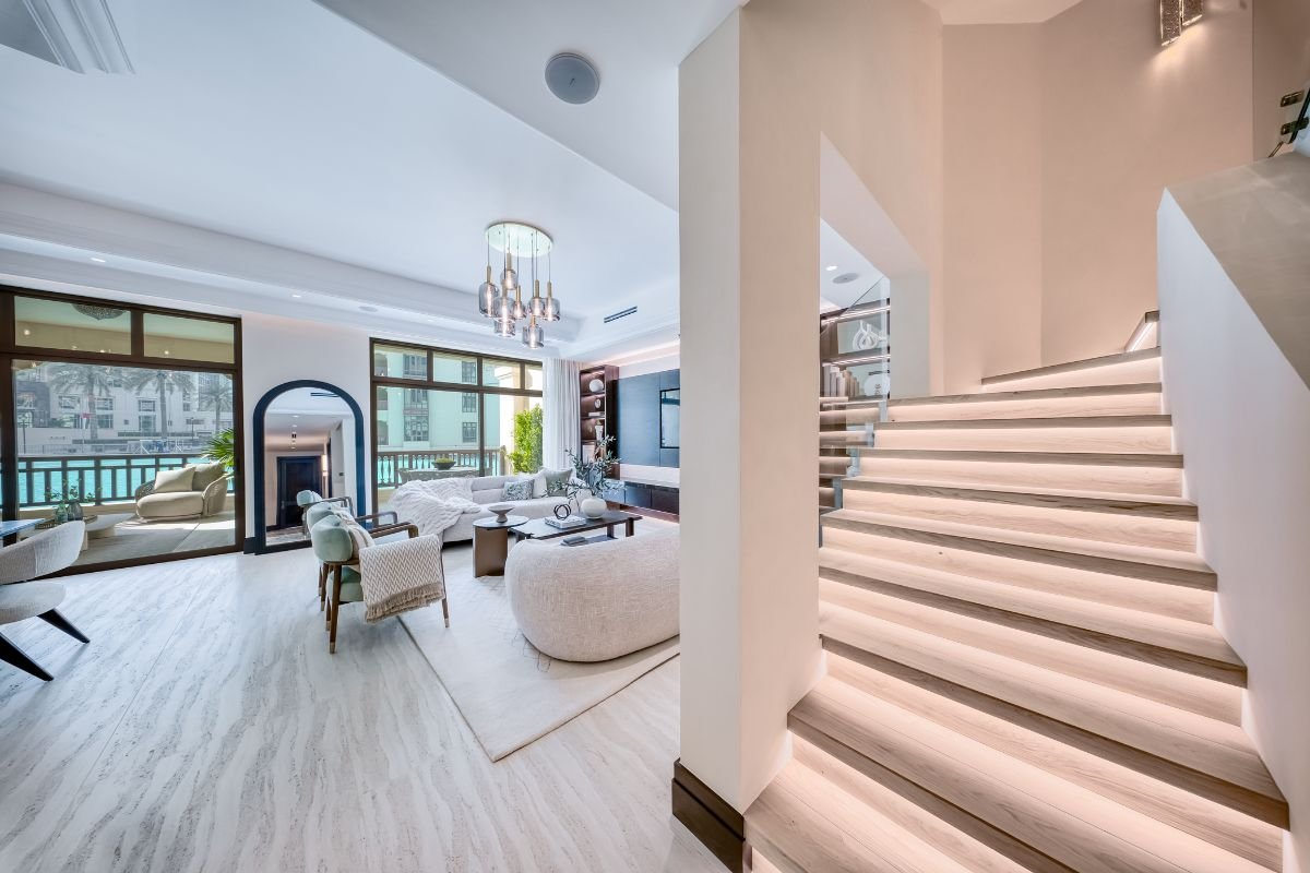 Modern staircase with integrated step lighting beside an elegant living area featuring neutral furnishings.