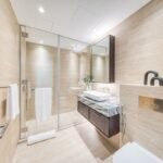 Luxury bathroom with beige stone walls, a glass-enclosed shower and marble-topped vanity unit.
