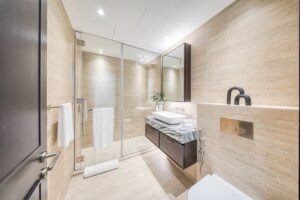 Luxury bathroom with beige stone walls, a glass-enclosed shower and marble-topped vanity unit.