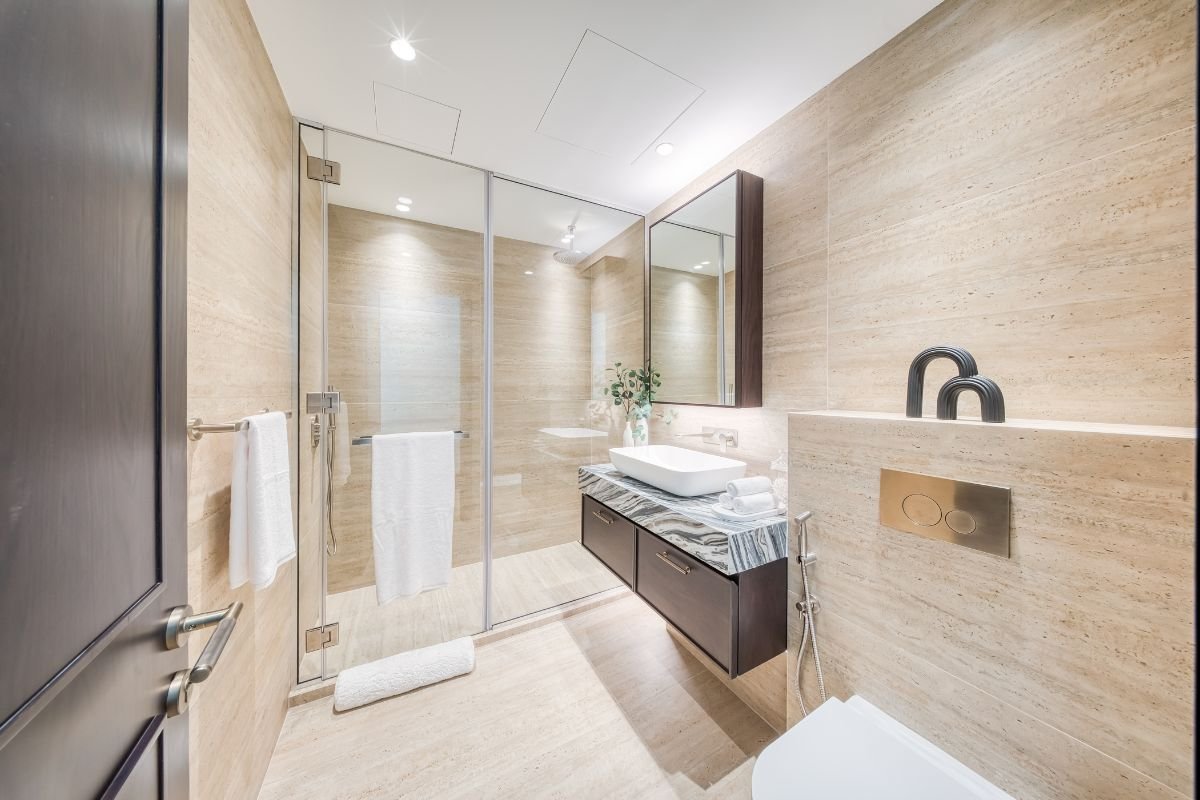 Luxury bathroom with beige stone walls, a glass-enclosed shower and marble-topped vanity unit.