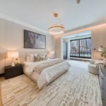 Spacious bedroom with an upholstered bed, chandelier and balcony doors overlooking the Downtown Dubai waterfront.